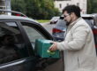 man handing green food bin through car window