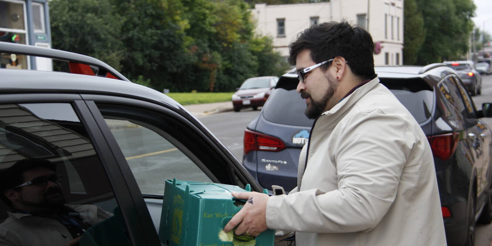 man handing green food bin through car window