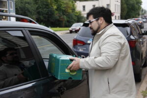 man handing green food bin through car window